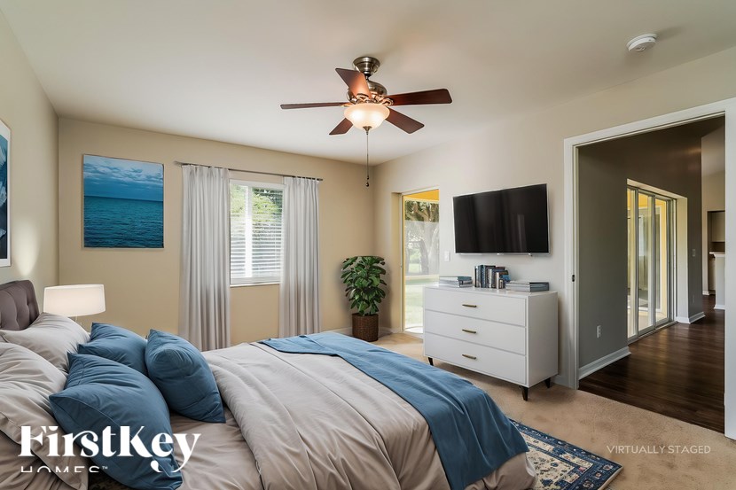 A bedroom with a bed, a ceiling fan, and a painting of the ocean on the wall.