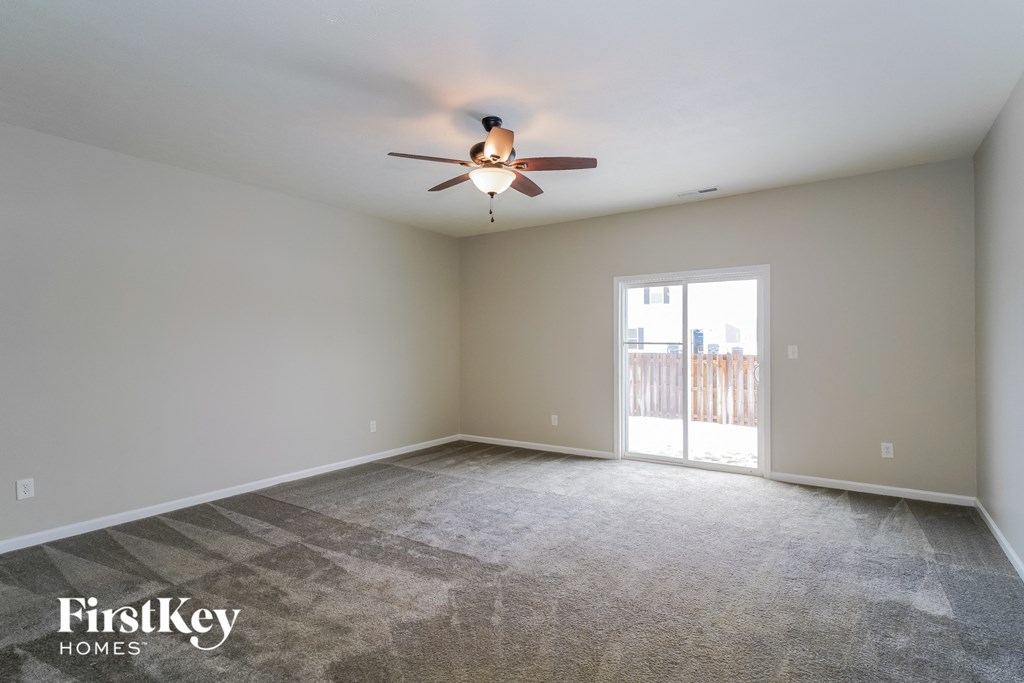 an empty living room with a ceiling fan and a door to a balcony