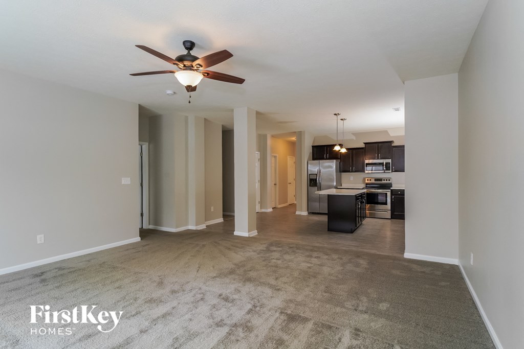 an empty living room with a ceiling fan and a kitchen