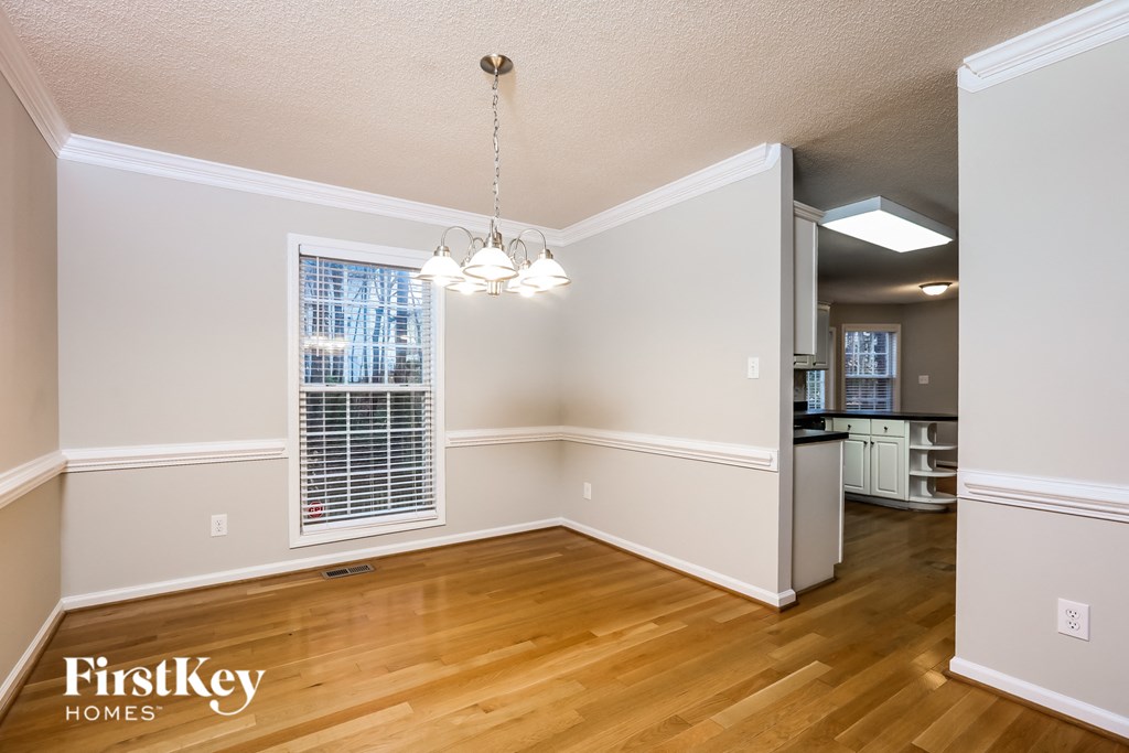 A well-lit, empty room with wooden floors and a chandelier hanging from the ceiling.