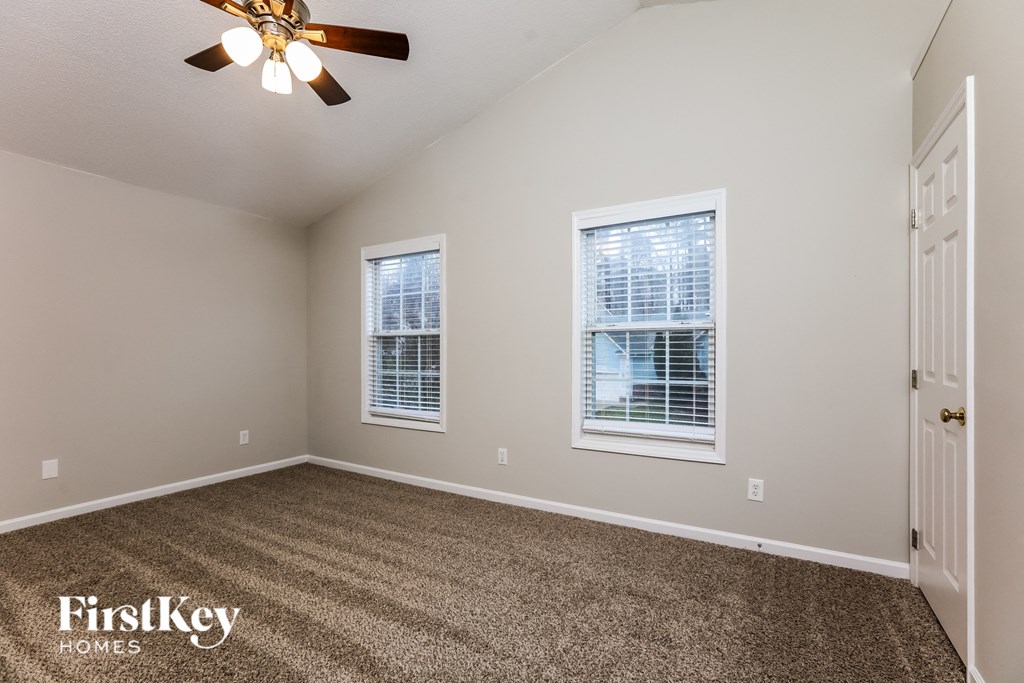 A room with a carpeted floor, a ceiling fan, and two windows.
