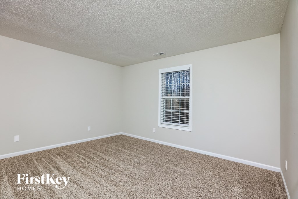 A room with a carpeted floor and a window with blinds.