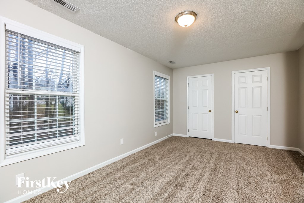 A room with a carpeted floor, two doors, and a window with blinds.