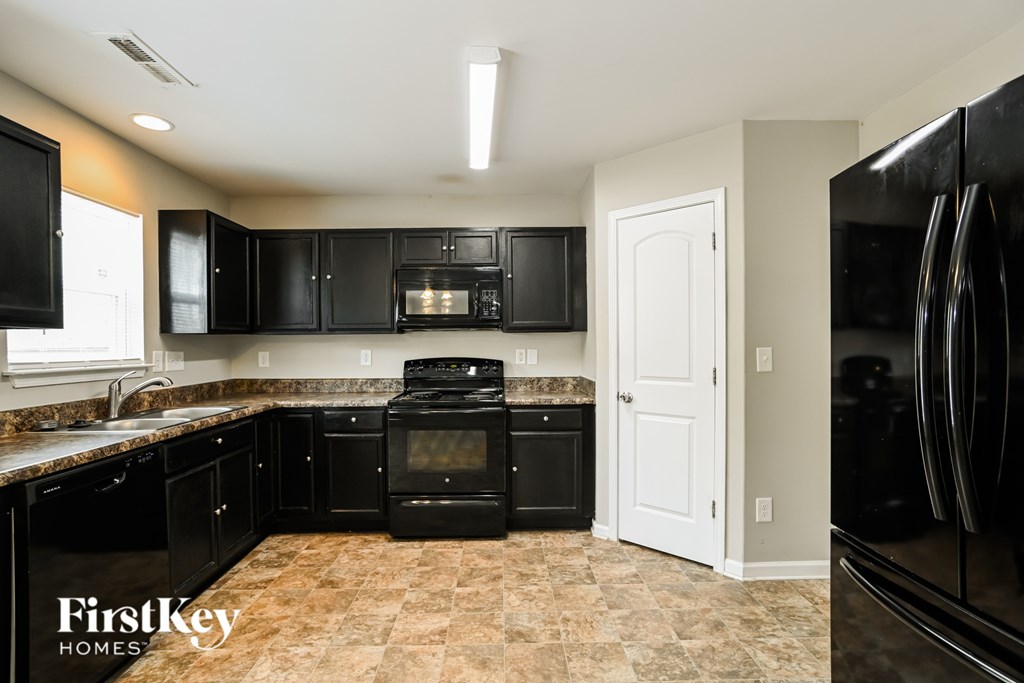 A kitchen with black appliances and a tile floor.