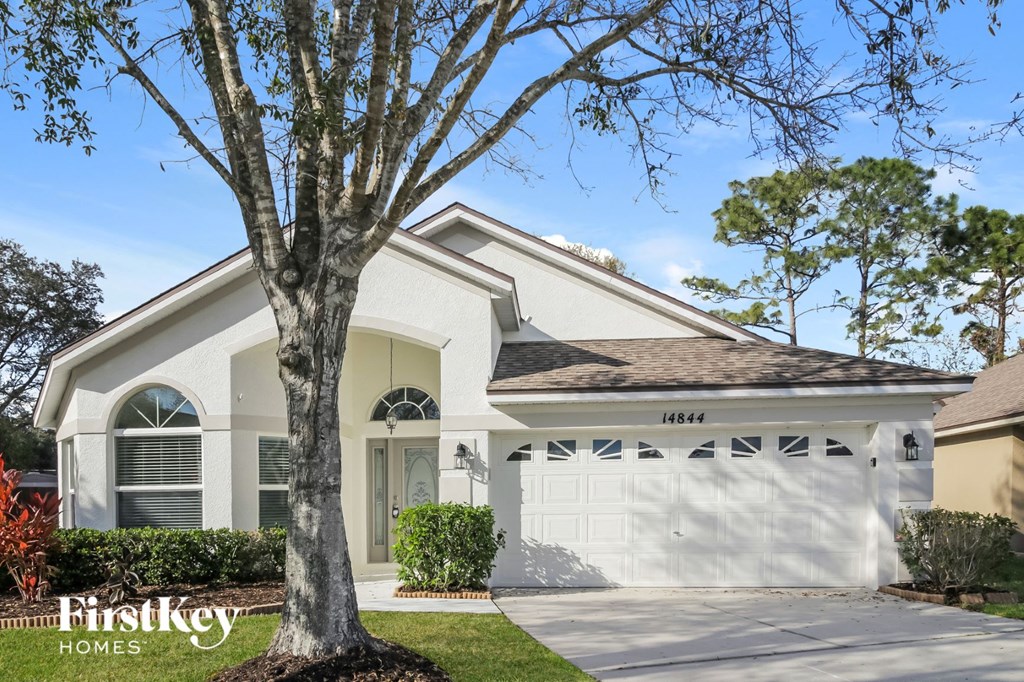 a white house with a white garage door and a tree