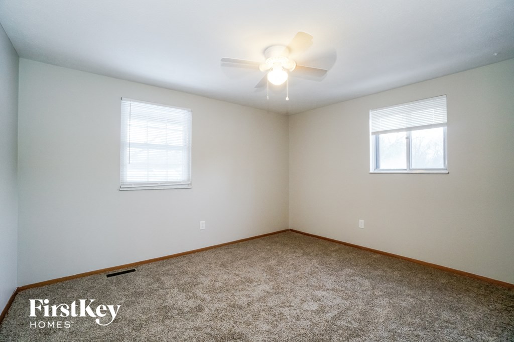 a bedroom with carpet and a ceiling fan and two windows