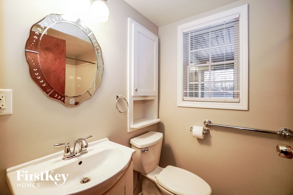 a bathroom with a sink toilet and mirror and a window