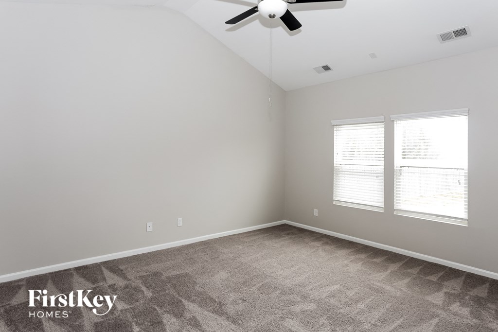 A room with a carpeted floor, a ceiling fan, and a window with blinds.