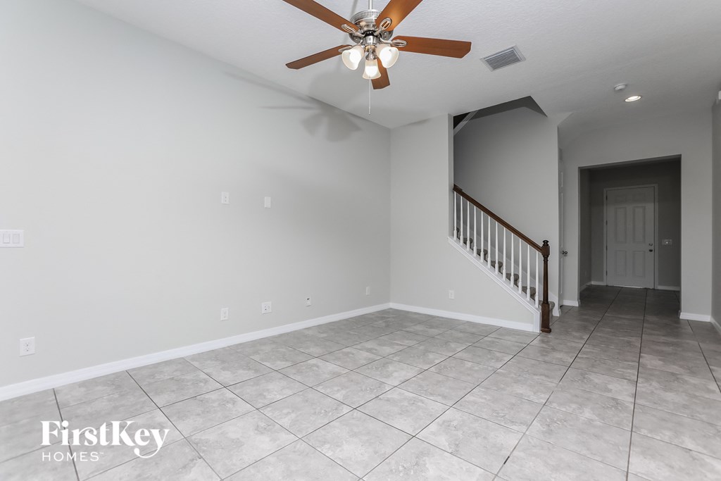 A spacious room with a staircase and a ceiling fan.