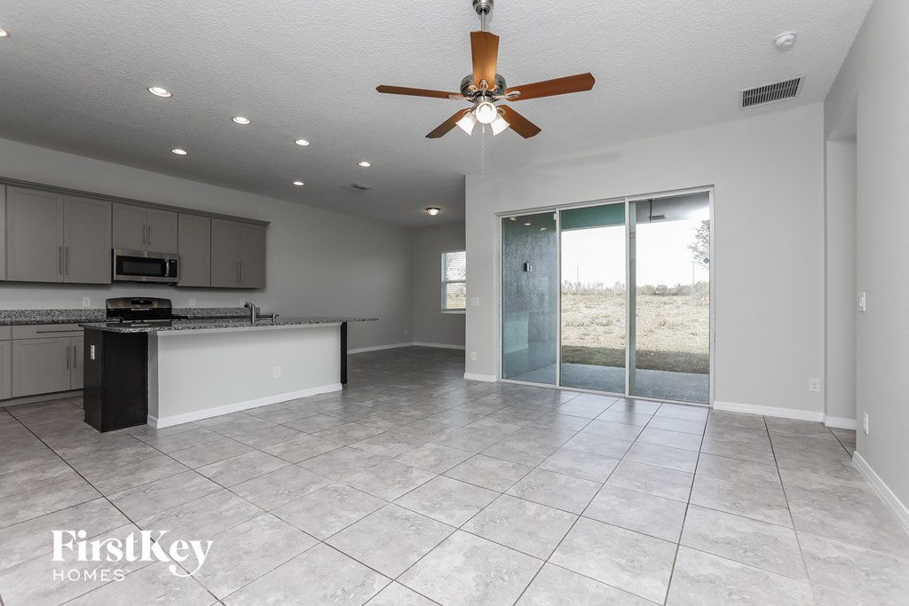 A spacious, empty room with a ceiling fan and a kitchen area with cabinets and a countertop.