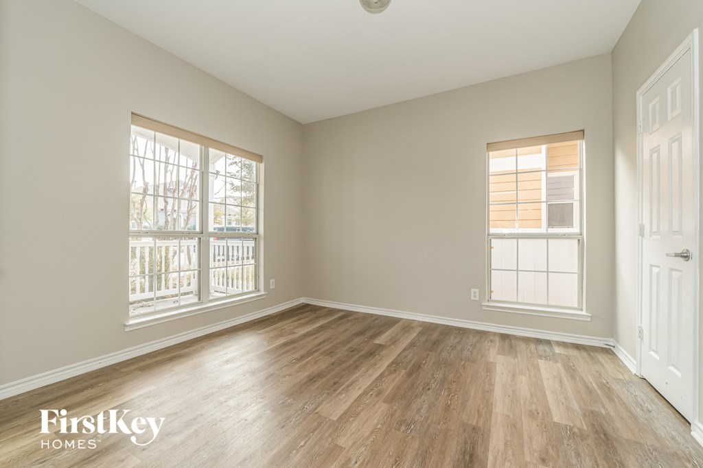 a spacious living room with hardwood floors and two windows