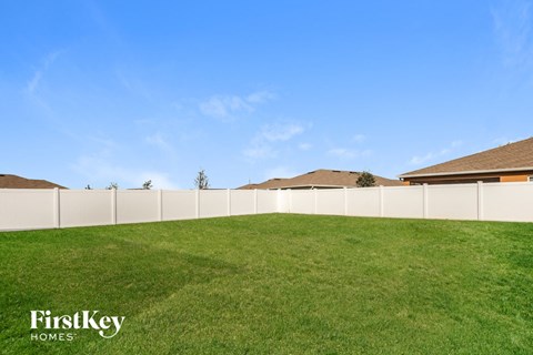 A grassy field with a fence and houses in the background.