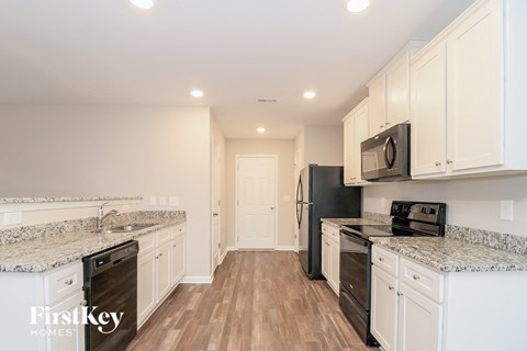 a kitchen with white cabinets and black appliances and marble counter tops