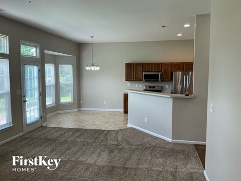 A spacious kitchen and living room with a carpeted floor and a large window.