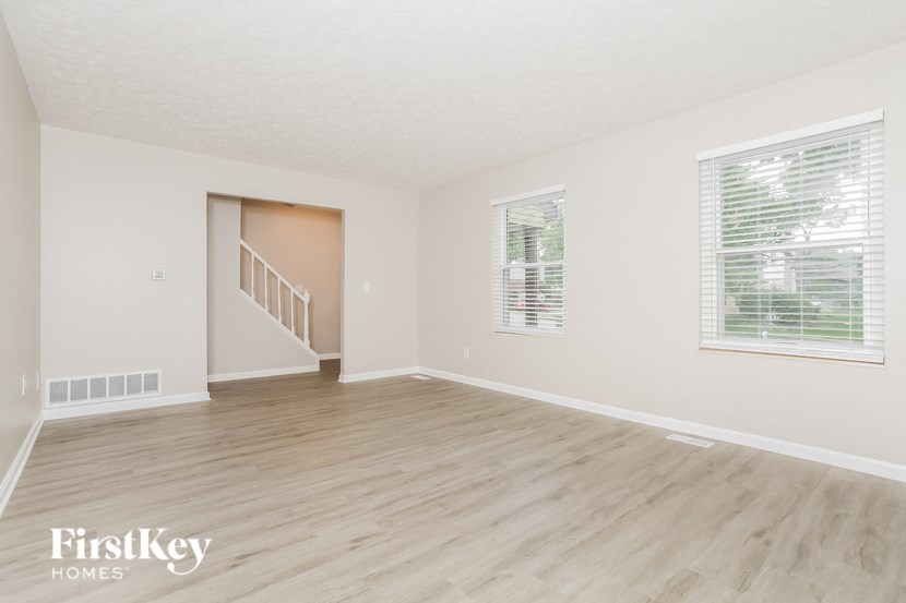 a spacious living room with hardwood floors and white walls and a staircase