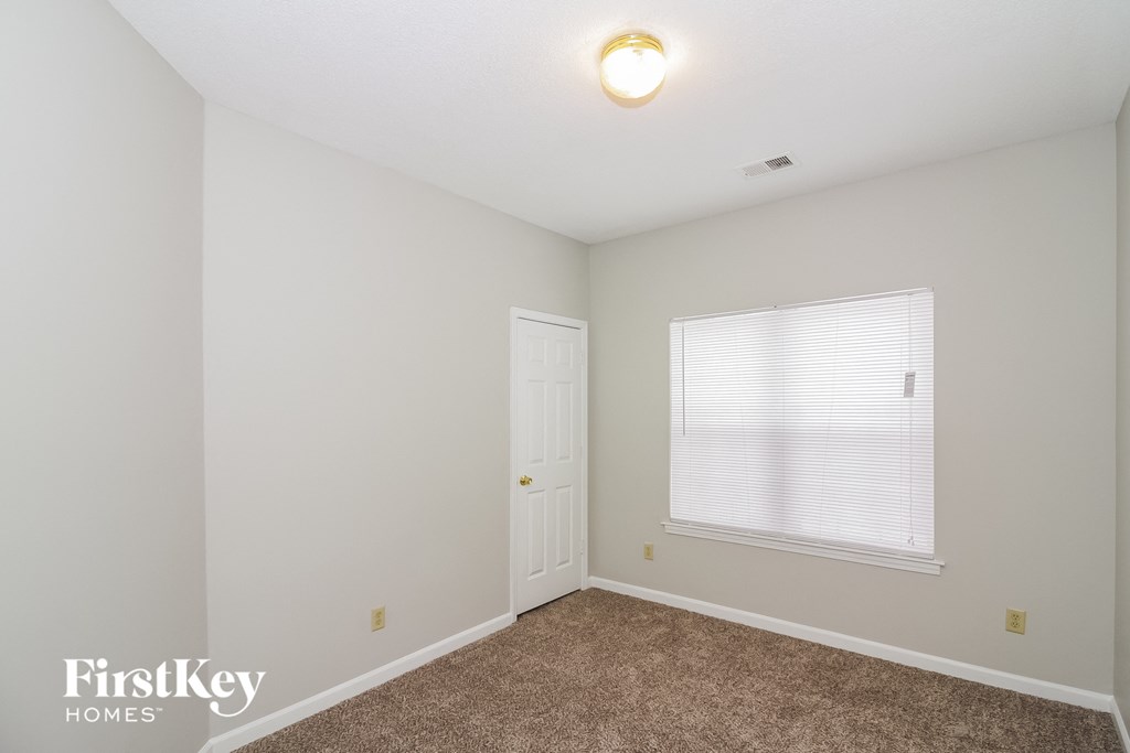 A room with a carpeted floor, a window with blinds, and a door.