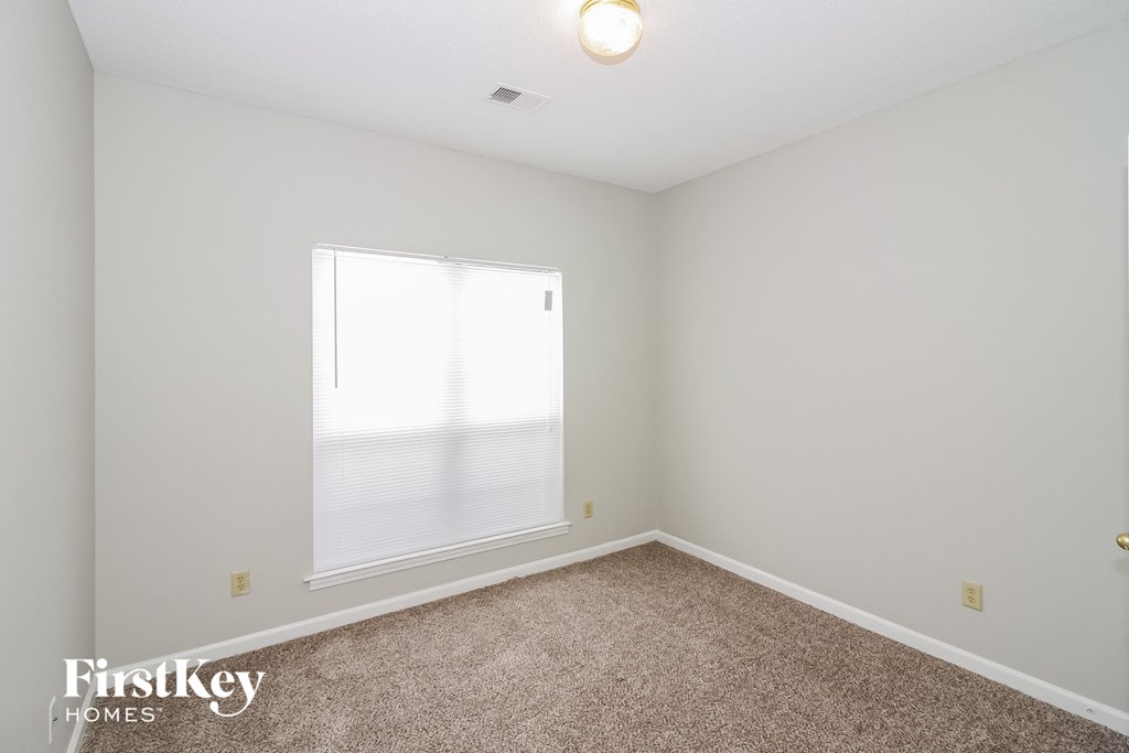 A room with a carpet floor and a window letting in light.