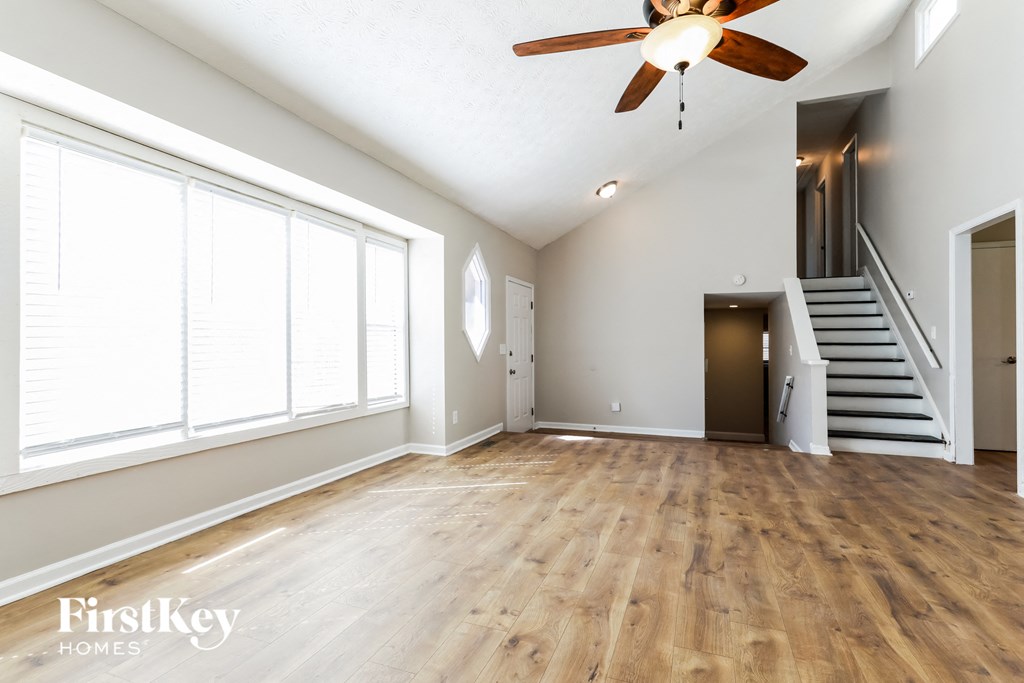 an empty living room with a ceiling fan and large windows
