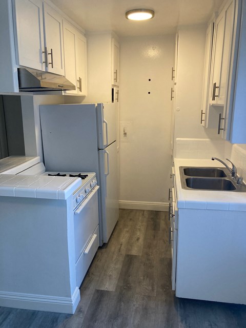 A white kitchen with a stove, refrigerator, and sink.