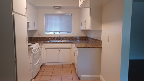 an empty kitchen with white appliances and a granite counter top