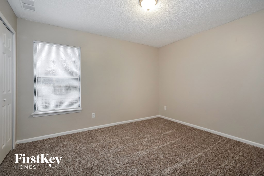 the spacious living room in this home has carpeting and a window