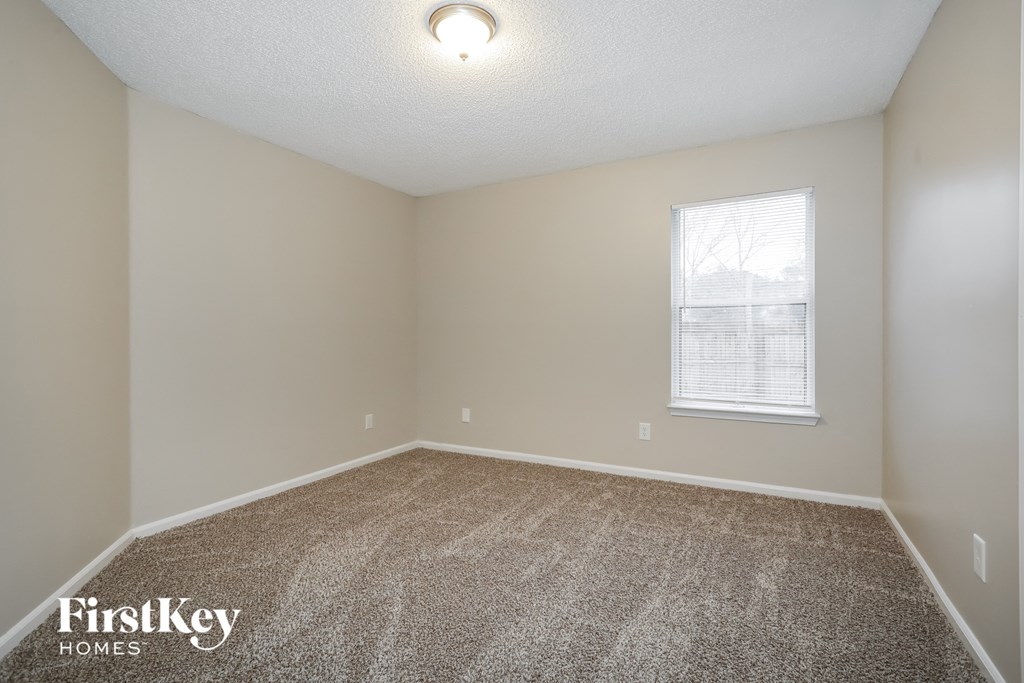 the spacious bedroom with carpeted flooring and a window