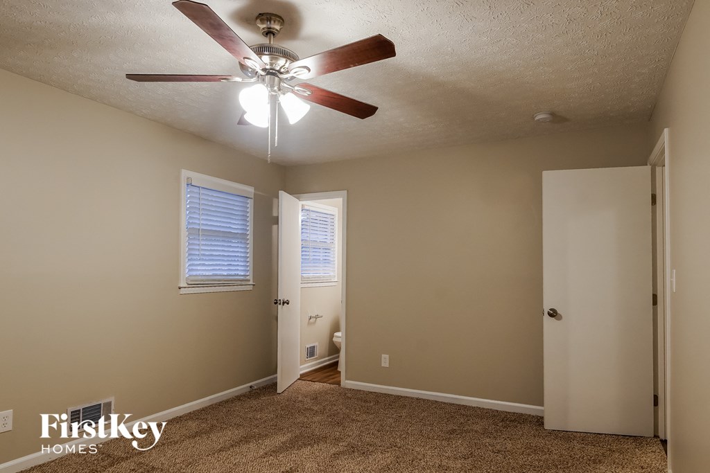 the living room has a ceiling fan and a door to the bathroom