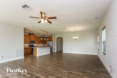 an empty living room with a ceiling fan and a kitchen