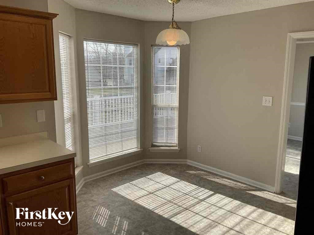 an empty living room with three windows and a kitchen