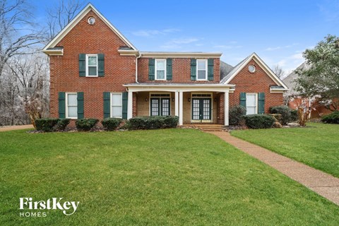 the front of a brick house with green shutters and a lawn
