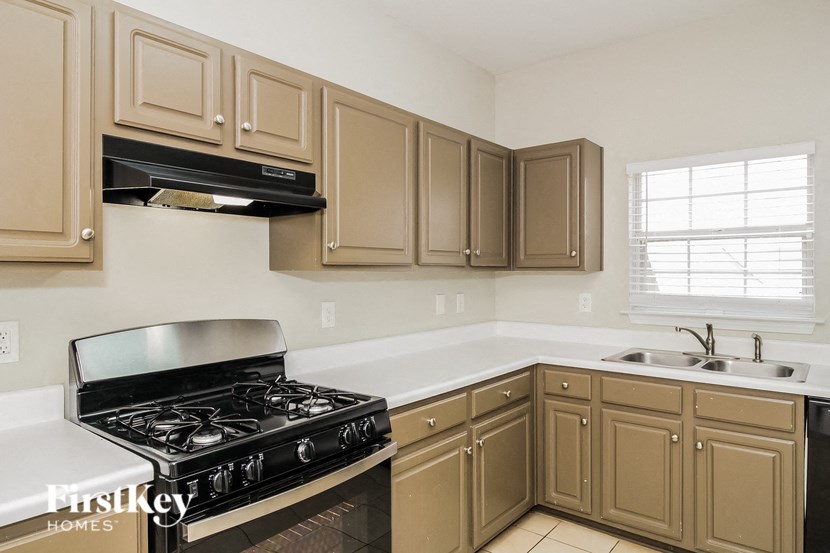 A kitchen with a black stove top oven and beige cabinets.