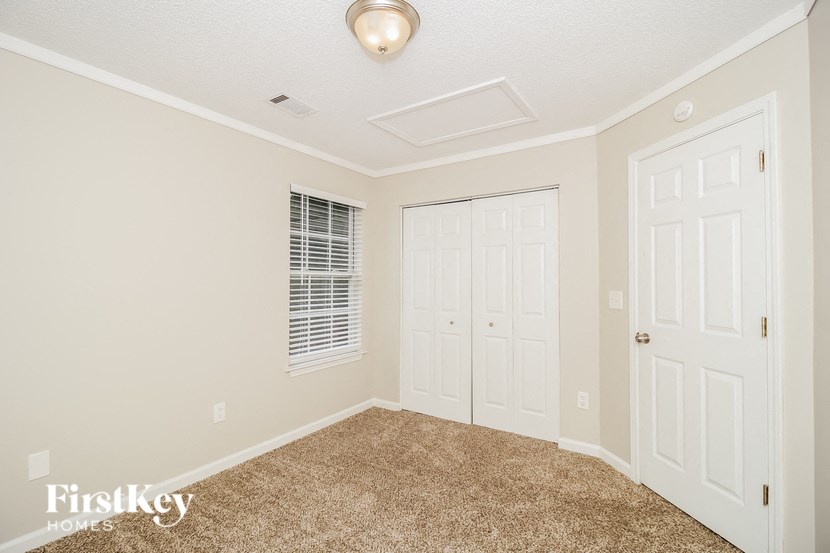 A room with a carpeted floor, two doors, and a window with blinds.