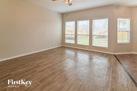A room with wooden flooring and three windows.