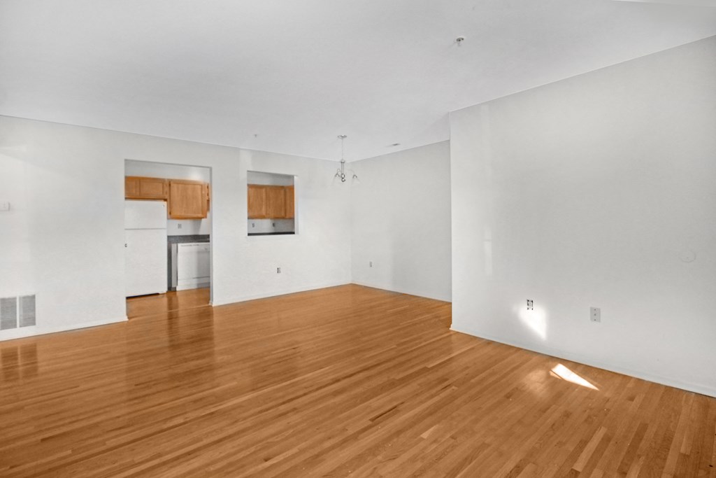 the living room and kitchen of an empty house with wood floors and white walls