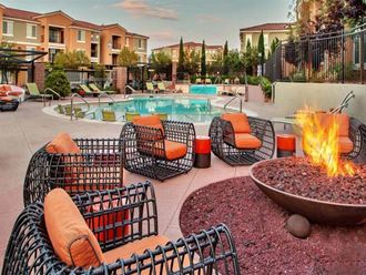 a pool with a fire pit and chairs in front of a swimming pool