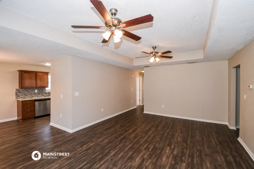 an empty living room with a ceiling fan and a kitchen