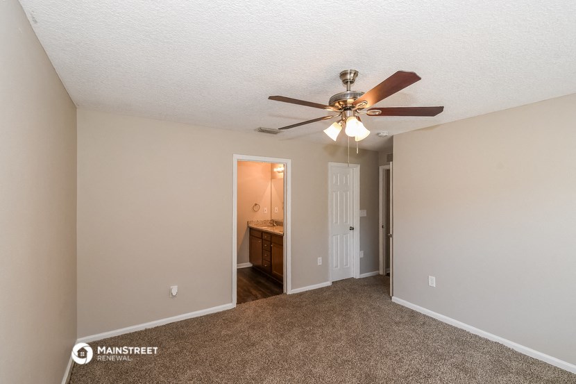 an empty living room with a ceiling fan and a door to a bathroom