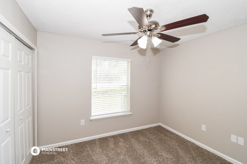 the spacious bedroom has a ceiling fan and carpet