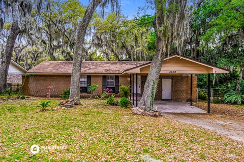 a small brick house with trees and a driveway