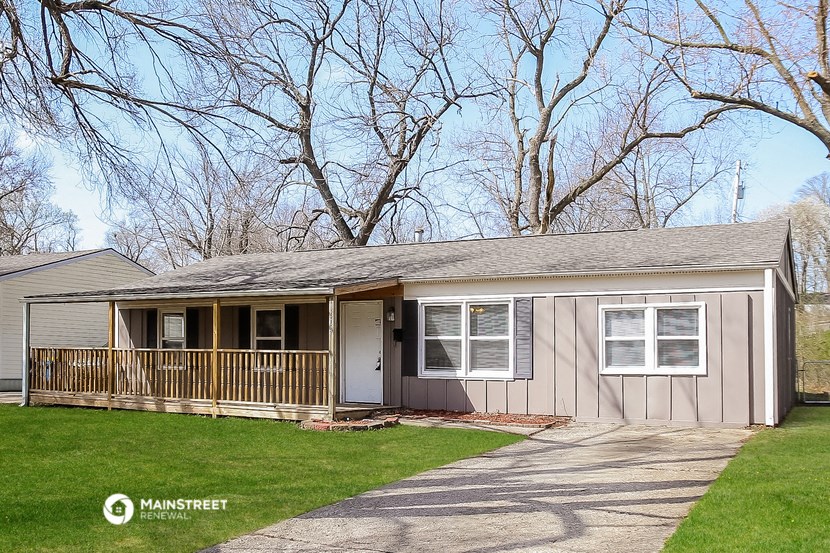 a small gray house with a porch and a yard