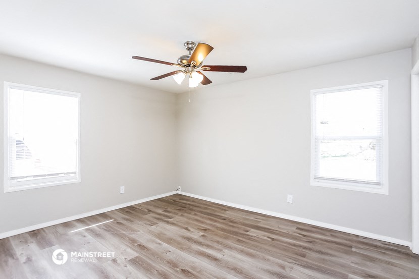an empty room with a ceiling fan and two windows