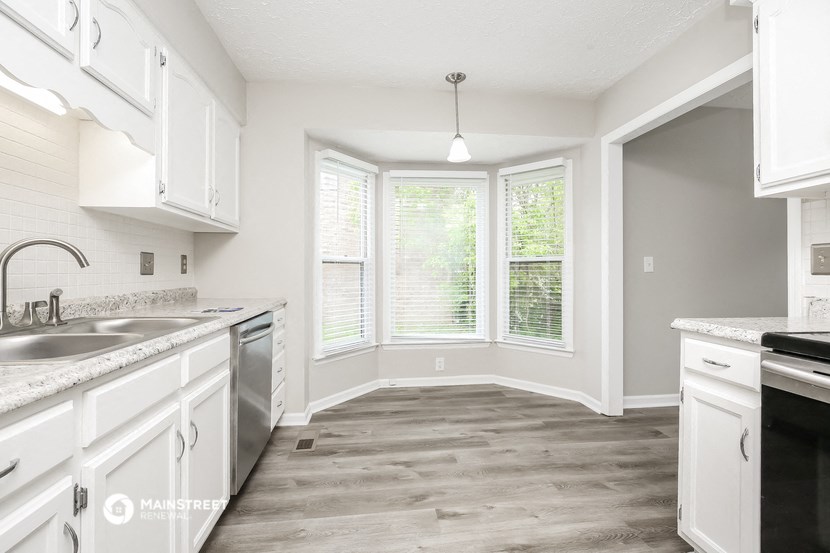 an empty kitchen with white cabinets and a large window