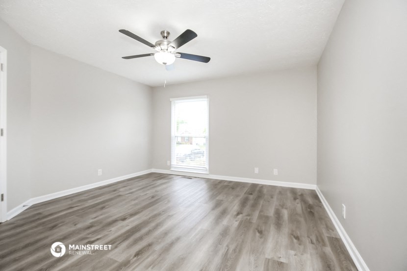 the spacious living room with hardwood flooring and a ceiling fan