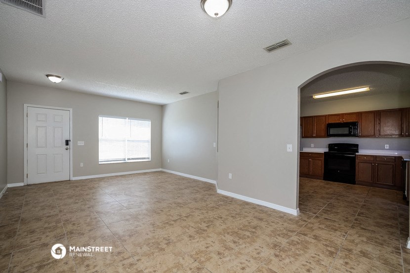 an empty living room with a white door and a kitchen