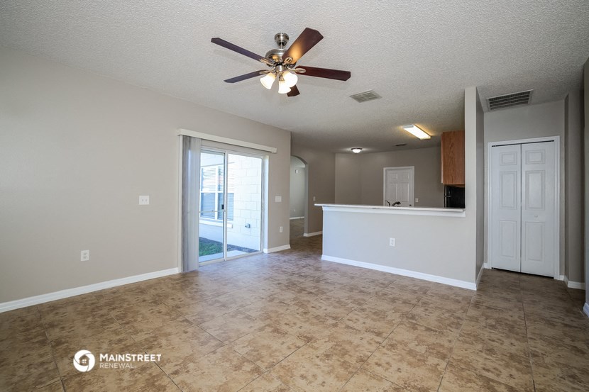 an empty living room with a ceiling fan and a kitchen