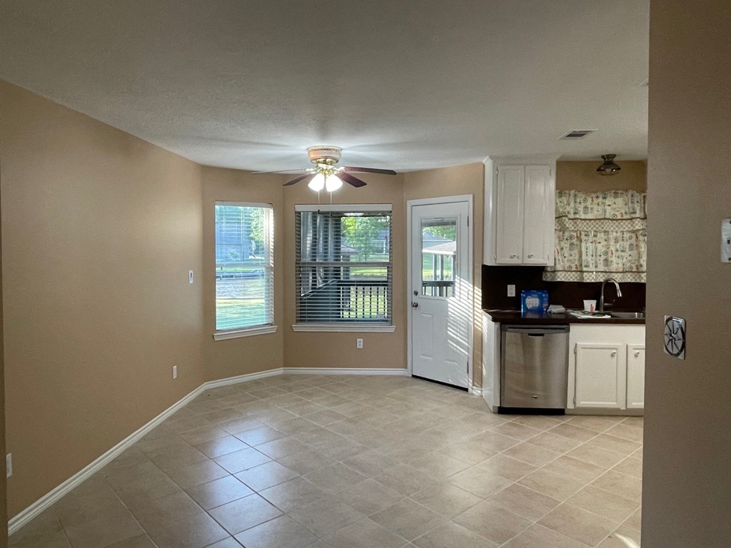 an empty living room with a kitchen and a ceiling fan