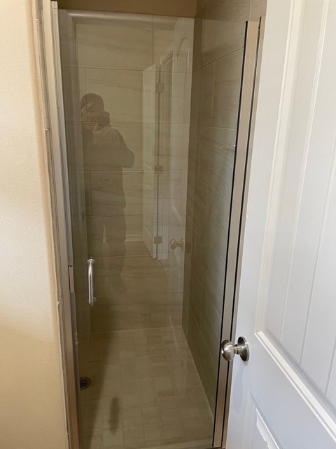 A person is taking a picture of a bathroom with a glass door.