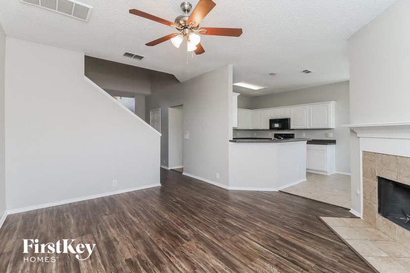 a living room and kitchen with a fireplace and a ceiling fan