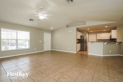 A spacious empty room with a kitchen area in the background.