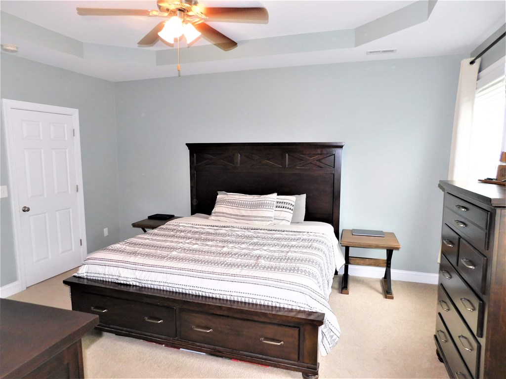 A bedroom with a bed, dresser, and ceiling fan.